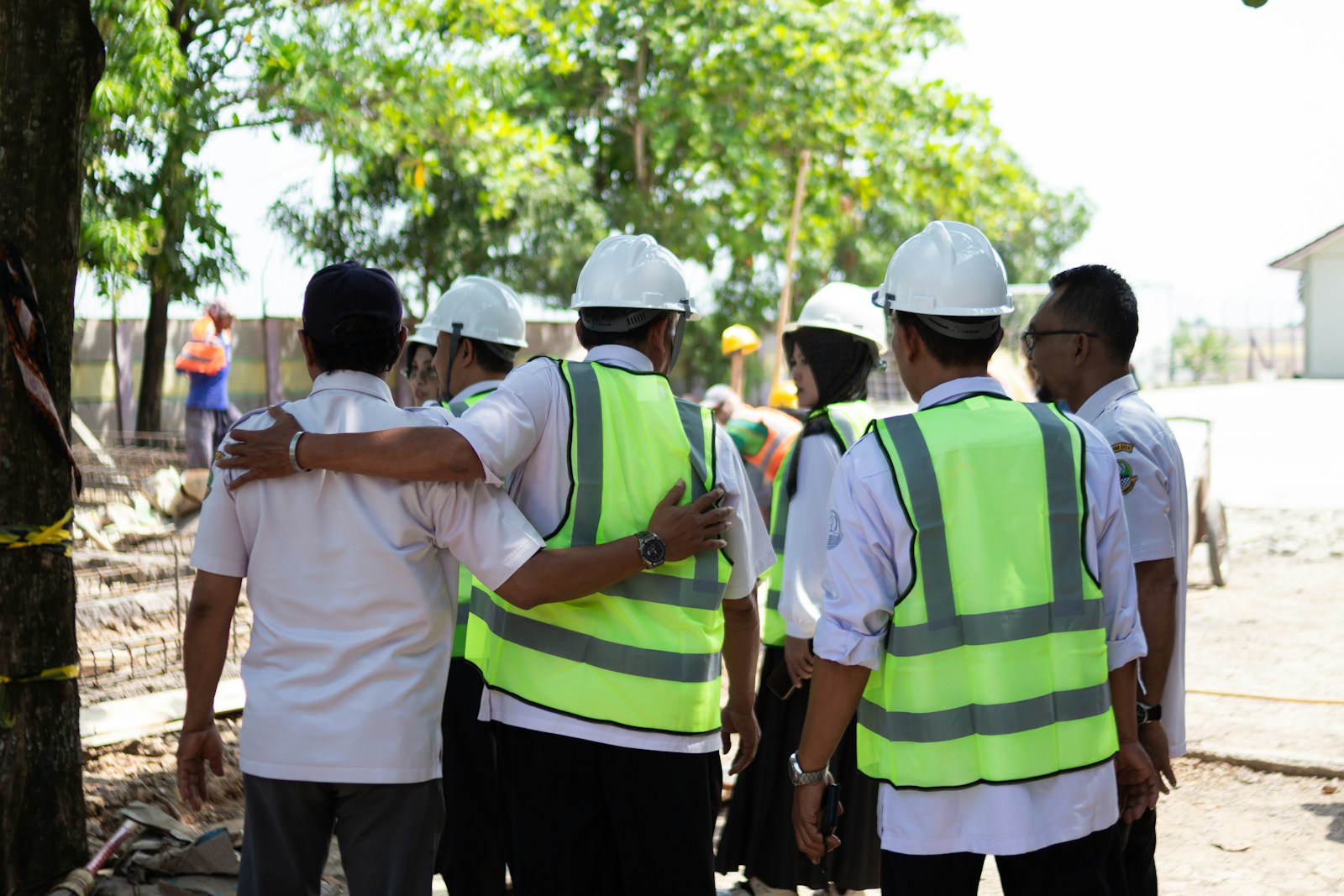 A group of construction workers in hard hats and reflective vests observes work at a site, emphasizing teamwork and safety in building projects.